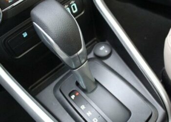 Desligar um carro automático pode parecer uma tarefa simples, mas se não for feito corretamente, pode causar danos significativos à transmissão e resultar em altos custos. Com a crescente popularidade dos carros automáticos no Brasil, é essencial que motoristas compreendam a maneira correta de desligar esses veículos para evitar prejuízos. Cometer erros como engatar a marcha em "P" (Parking) antes de o carro estar completamente parado pode comprometer o funcionamento a longo prazo. Entendendo os Riscos Os problemas ao desligar um carro automático de forma inadequada não se limitam apenas à transmissão. Engates errados podem causar trancos e desgastes prematuros. Em declives, acionar o "P" antes do freio de mão pode sobrecarregar o sistema, levando a avarias. Além disso, motoristas de carros com motor turbo devem esperar alguns segundos antes de desligar o motor para proteger o sistema de lubrificação. Procedimento Correto para Desligar Para garantir a segurança e a longevidade da transmissão, siga o procedimento correto de desligamento: Certifique-se de que o veículo está totalmente parado. Mantenha o pé no freio e mude a alavanca para "N" (Neutro). Acione o freio de mão, garantindo que o peso do carro seja suportado adequadamente. Engate a alavanca em "P". Desligue o motor. Esta sequência não só preserva a transmissão como também aumenta a segurança ao estacionar. Evitando Falhas Futuras Entender os riscos associados ao desligamento inadequado ajuda a evitar falhas no carro. Práticas incorretas podem afetar componentes elétricos e resultar em mensagens de erro no painel. O uso correto da posição "N" e a sequência apropriada são essenciais para evitar trancos em superfícies inclinadas e para preservar o funcionamento do veículo. Benefícios de Pequenos Cuidados Adotar práticas corretas ao desligar um carro automático é mais do que uma questão de evitar reparos dispendiosos. É um investimento na longevidade e eficiência do veículo. Com motoristas cada vez mais optando por modelos automáticos, o conhecimento das melhores práticas de desligamento se torna indispensável. Informações adequadas e a implementação desses cuidados no dia a dia podem prevenir muitos problemas futuros e garantir que seu carro esteja sempre em ótimas condições de uso. Em outubro de 2023, o aumento da frota de veículos automáticos no Brasil destaca a importância de seguir esses passos corretos de desligamento. Proteger seu investimento e garantir uma condução mais tranquila são razões suficientes para adotar essas práticas.