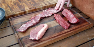 Lugar da sua cozinha está infestado de bactérias e você coloca comida nele todo dia Seja de madeira, bambu, vidro, plástico ou inox, cada tipo de tábua requer cuidados específicos para manter a higiene adequada. A higienização correta das tábuas de cozinha é fundamental tanto em cozinhas domésticas quanto em profissionais, onde a contaminação cruzada pode ocorrer. Garantir a segurança alimentar é a principal razão para seguir métodos adequados de desinfecção, além de contribuir para a longevidade do utensílio. A importância da limpeza correta das tábuas Entender a importância da limpeza regular é o primeiro passo para garantir que sua tábua de cozinha permaneça livre de contaminação. Durante o uso diário, a tábua de corte acumula resíduos de diversos alimentos, tornando-se um potencial vetor para bactérias perigosas. Dessa forma, a higienização não só previne contaminação, mas também aumenta a durabilidade dos materiais de que é feita. Métodos de desinfecção para tábuas de madeira e bambu Tábuas de madeira e bambu são populares, mas exigem cuidados específicos devido à sua porosidade. Recomenda-se lavar com detergente neutro e água corrente usando uma esponja macia. Após a lavagem, é crucial permitir que sequem completamente em um local ventilado, longe da luz solar direta para evitar rachaduras. Para uma desinfecção mais profunda, misture uma solução de uma colher de sopa de água sanitária para cada galão de água, aplicando na tábua com um pano e deixando agir por apenas 2 minutos antes de enxaguar. Higienizando tábuas de plástico e vidro As tábuas de plástico podem ser lavadas na lava-louças, mas é recomendável deixá-las de molho em uma solução de água sanitária antes, para garantir que as ranhuras também sejam limpas. Uma solução eficaz para manchas e odores é a combinação de bicarbonato de sódio e limão: polvilhe bicarbonato na superfície, esfregue com meio limão, deixe agir e enxágue bem. Já as tábuas de vidro necessitam apenas de uma lavagem com detergente comum e água, sendo fáceis de higienizar, porém cuidar do fio das facas é essencial devido à superfície dura do vidro. Cuidados específicos com tábuas de inox As tábuas de inox, usadas eventualmente em cozinhas, não devem ser expostas à água sanitária, pois isso pode provocar corrosão. O melhor método é usar água e detergente, sempre enxaguando completamente. Mantenha-as longe de substâncias abrasivas que possam comprometer sua superfície. Independentemente do tipo de tábua, práticas gerais de manutenção incluem raspar os resíduos logo após o uso e armazenar em locais secos e arejados. Isso impede que bactérias e fungos se desenvolvam. Escolhendo a tábua ideal para sua cozinha A escolha da tábua ideal deve considerar o uso pretendido e a facilidade de limpeza dos materiais. Conhecendo as propriedades específicas de cada material, você pode decidir qual atende melhor seus requisitos sem comprometer a segurança dos alimentos preparados. Aplicando essas práticas, não apenas protege-se a sua cozinha, mas também se preserva a saúde daqueles que compartilham as refeições. Uma boa rotina de limpeza não apenas minimiza riscos, como também garante a longa vida útil das tábuas de corte. A correta desinfecção e manutenção preventiva são passos essenciais para manter o ambiente da sua cozinha mais higiênico e seguro.