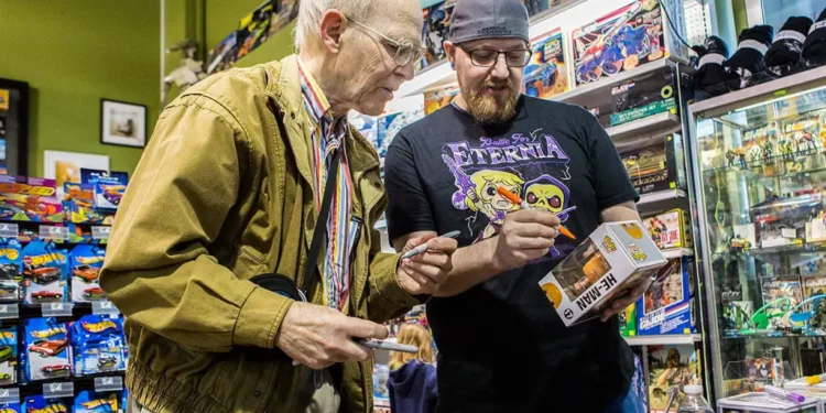 Sweet (à esquerda) assinando um Funko Pop do He-Man.

Reprodução: Olivia Vanni / The Herald